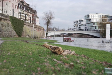 Eine Sitzbank am Gehweg des Donauufers wird von Wasser umspült.