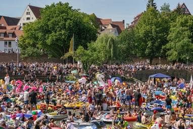 Viele Menschen feiern in Schlauchbooten auf der Donau. Einige der Boote haben die Form eines Einhorns oder eines Flamingos.
