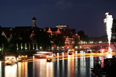 Bei Nacht spiegeln sich zahlreiche Lichter auf der Donau im Wasser.