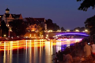 Am Ufer beobachten Zuschauer die auf der Donau schwimmenden Lichter.