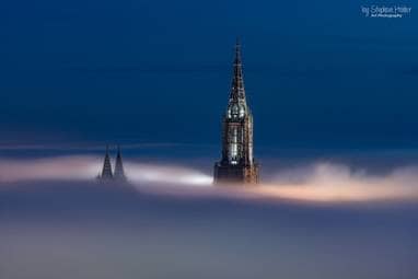 Der Hauptturm des Münster und die beiden Chortürme ragen aus dem Nebel in den Himmel empor.