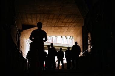 Menschen laufen durch einen dunklen Tunnel, an dessen Ende das Tageslicht hereinscheint.