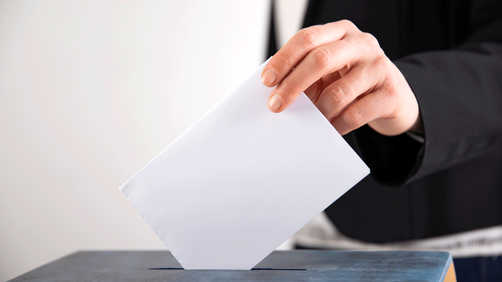 Eine Person steckt ihren Wahlbrief in eine Wahlurne.